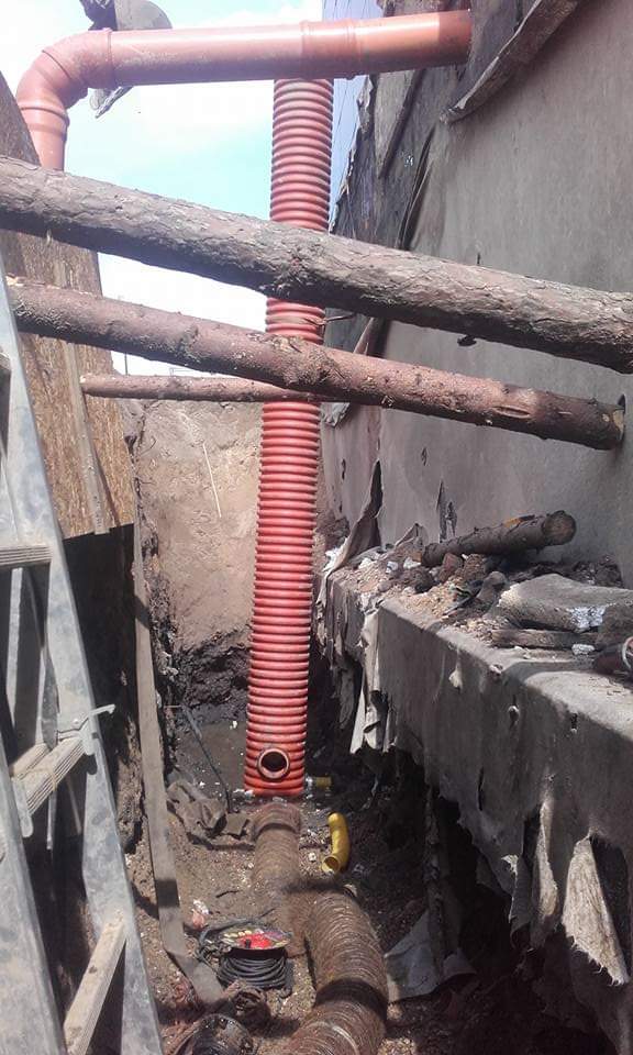 Wykop z widocznymi rurami kanalizacyjnymi z tworzywa sztucznego, zabezpieczony drewnianymi belkami, drabina oparta o ścianę wykopu.