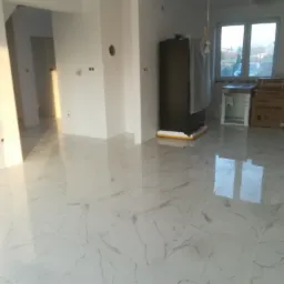 Jasne, marmurowe płytki podłogowe w przestronnym, nowo wykończonym wnętrzu z widocznymi przygotowaniami do montażu sprzętu AGD.