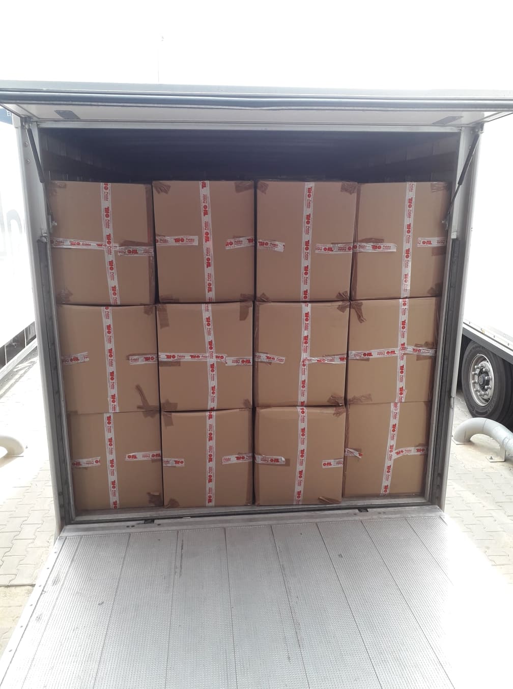 Kartonowe pudła zabezpieczone taśmą ułożone warstwami w przestrzeni ładunkowej pojazdu dostawczego z otwartymi drzwiami.