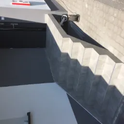 Zewnętrzne schody wyłożone szarymi płytkami, prowadzące do ciemnych drzwi wejściowych, z widoczną zwiniętą liną i drabinką w tle.