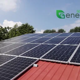 Panel słoneczny na czerwonym dachu z logo Go Green Energy na tle błękitnego nieba i zielonych drzew.
