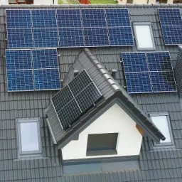 Instalacja paneli słonecznych na dachu domu z szarą dachówką, widok z góry, komin z cegły w tle.