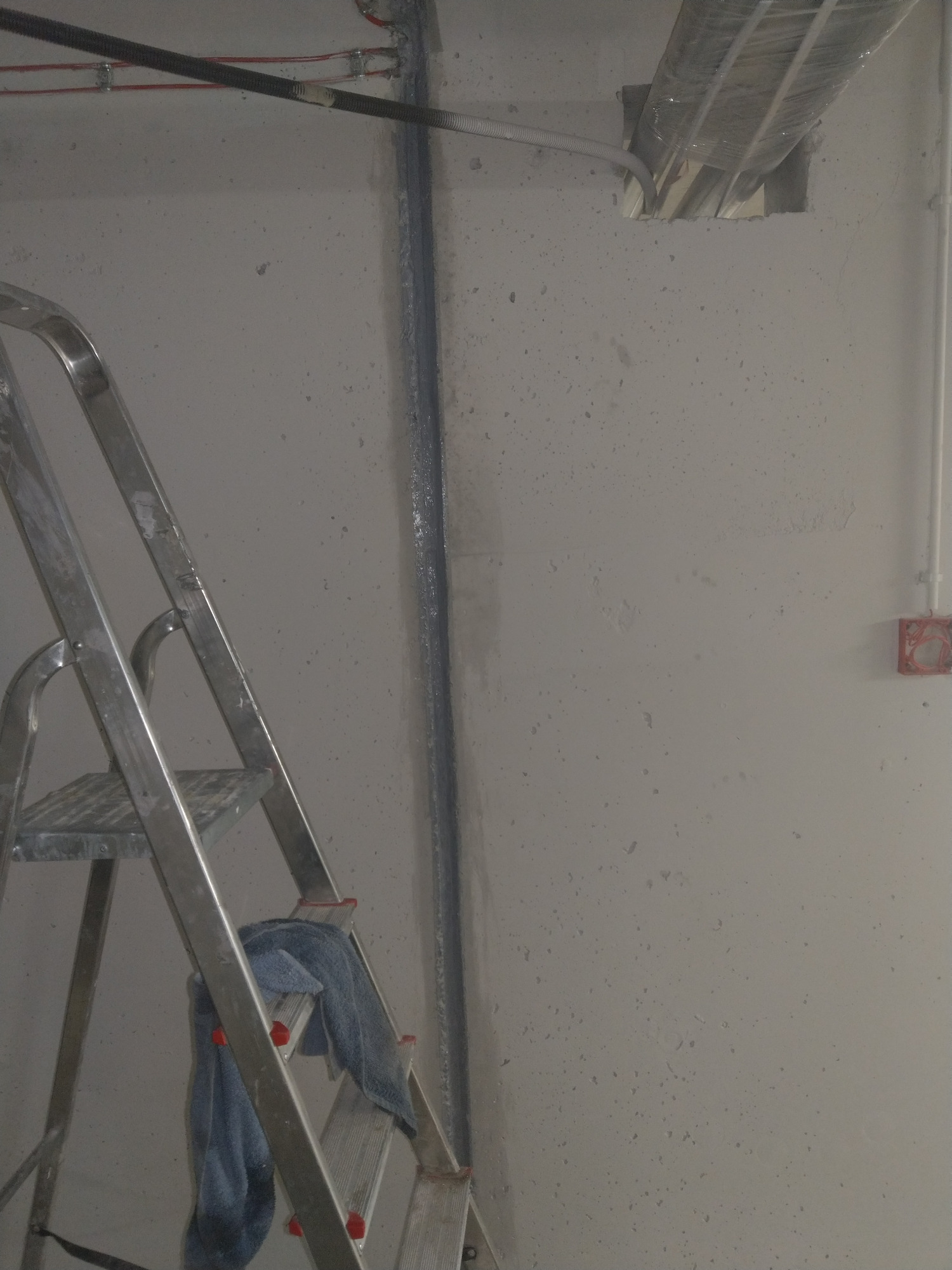 Świeżo położona instalacja elektryczna w korycie na ścianie, widoczna drabina aluminiowa z szmatką i puszką elektryczną w tle.