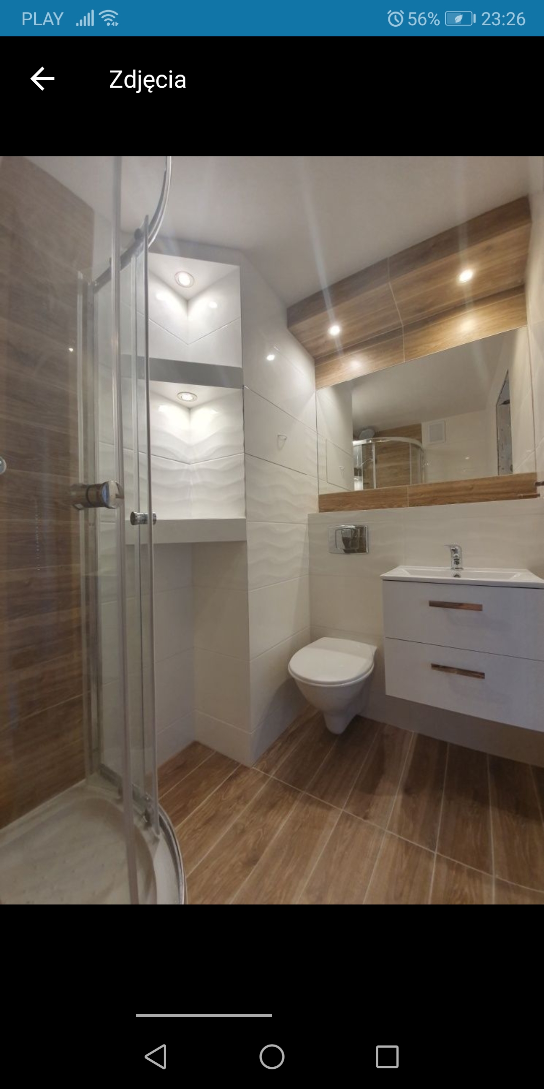 Nowoczesna łazienka z kabiną prysznicową, umywalką z szafką i toaletą; dominują płytki imitujące drewno i białe płytki ze strukturą fal