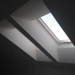 Dwa okna dachowe osadzone w białych, ukośnych wnękach w ciemnoszarym suficie poddasza, widok od dołu.