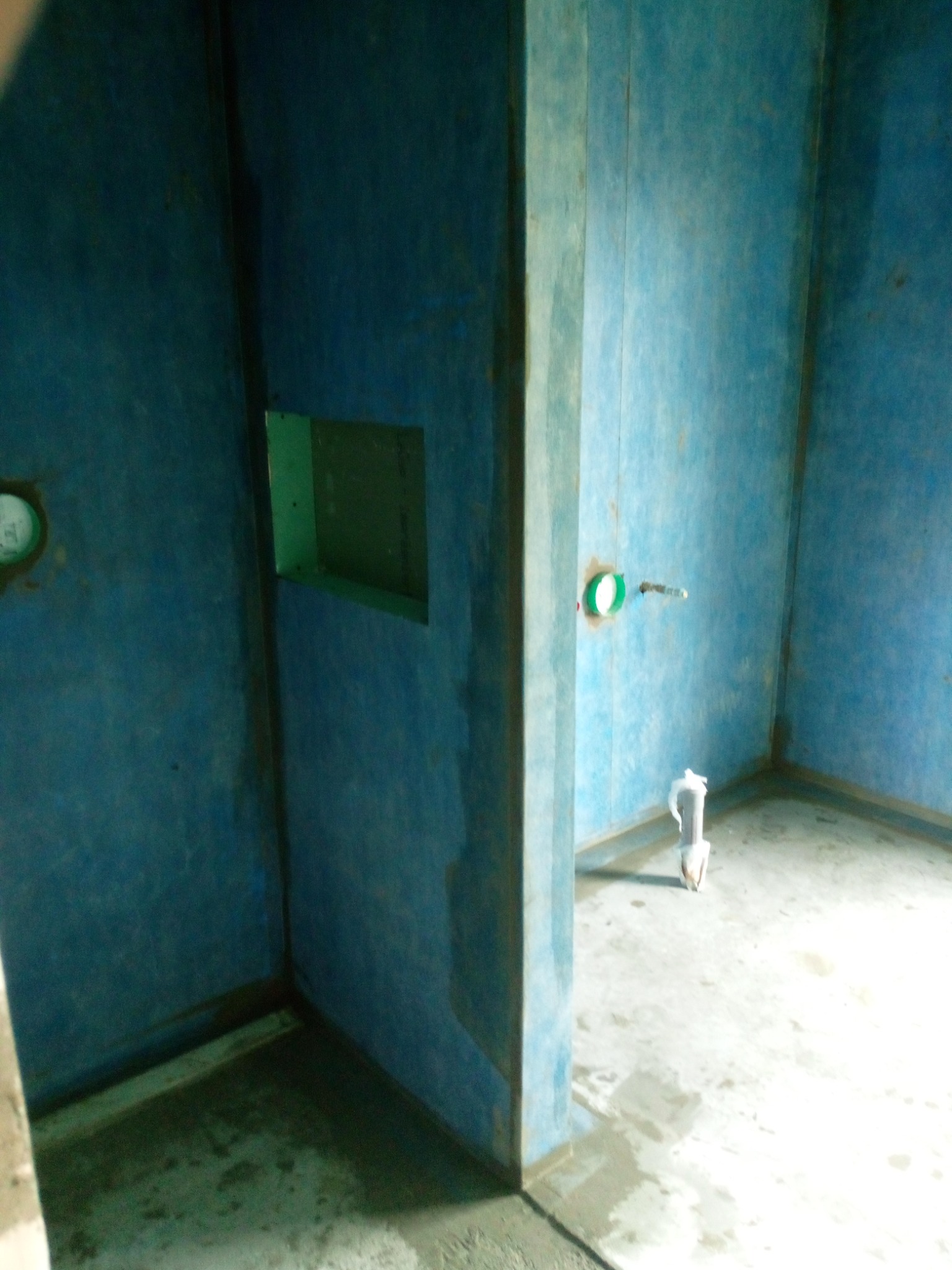 Przygotowanie do układania płytek w łazience, ściany zabezpieczone niebieską folią hydroizolacyjną, widoczny otwór na półkę i wystająca rura instalacji wodnej.