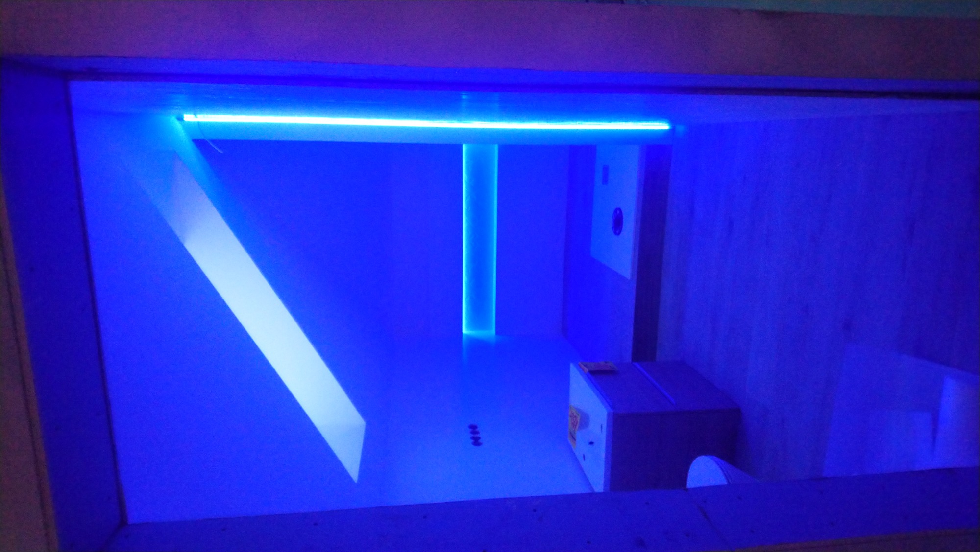 Nowoczesna łazienka w trakcie remontu z podświetleniem LED w kolorze niebieskim, widoczne elementy konstrukcyjne i przygotowane miejsce na umywalkę.