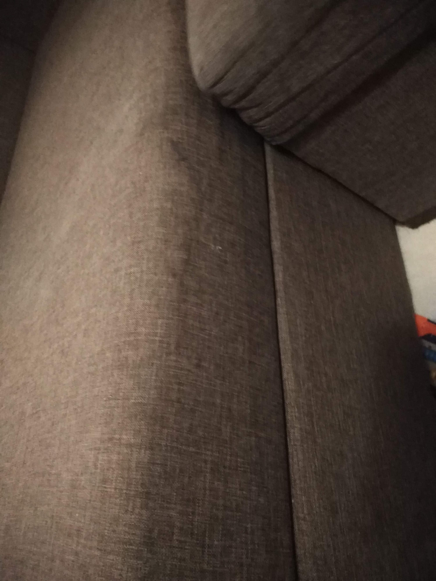 Fragment ciemnoszarej kanapy z widoczną fakturą materiału i szwem łączącym elementy tapicerki.