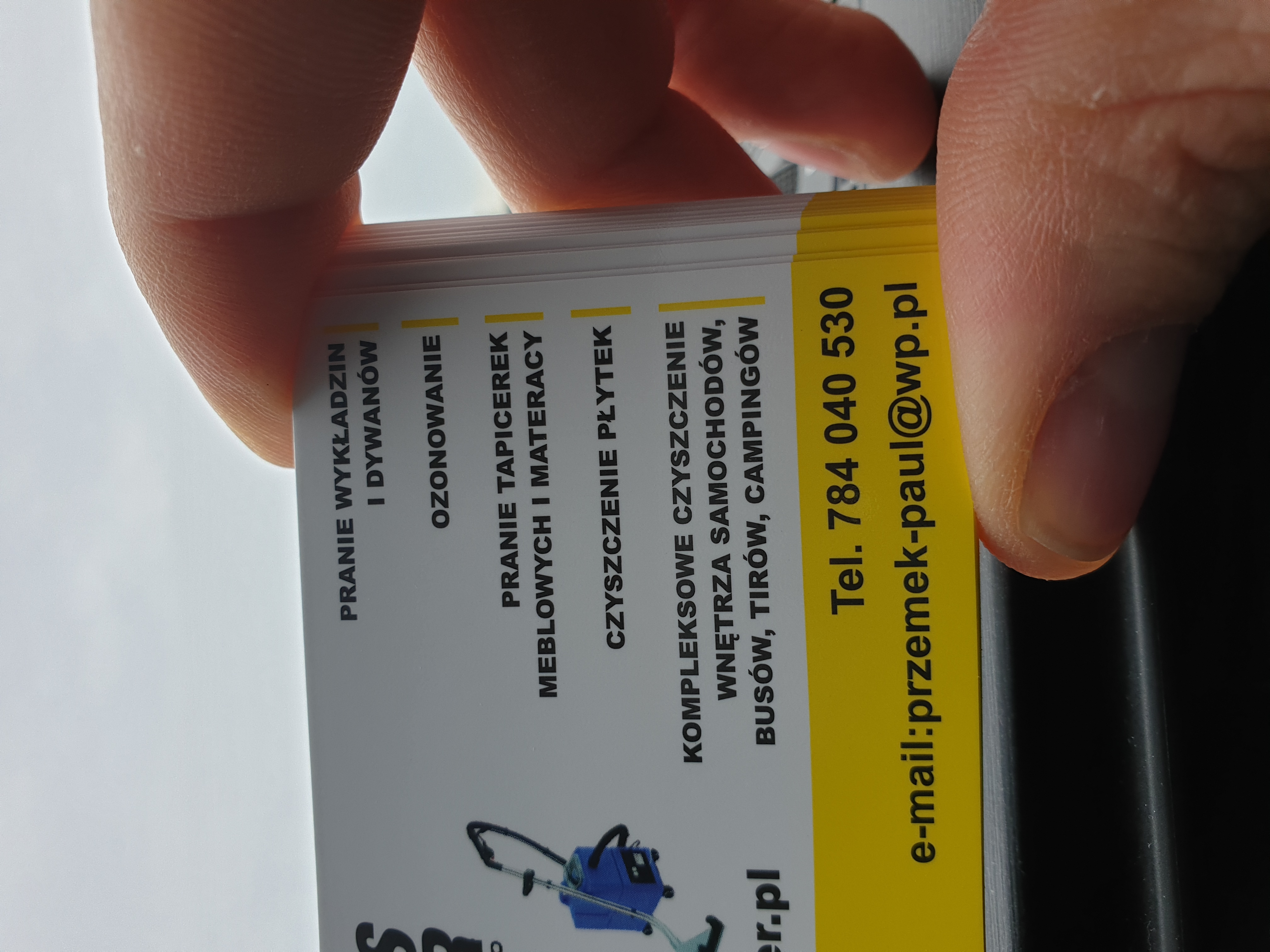 Stos wizytówek z ofertą prania wykładzin, dywanów, tapicerek meblowych oraz czyszczenia płytek i wnętrz samochodów, trzymany w palcach.