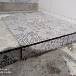 Układanie szaro-białych płytek podłogowych z wzorem patchworkowym w łazience, widoczne krzyżyki dystansowe i narzędzia glazurnicze.