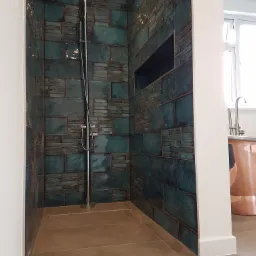 Kabina prysznicowa w Goleniowie z turkusowymi, błyszczącymi płytkami ułożonymi w nieregularny wz&oacute;r, z wnęką w ścianie i chromowaną armaturą, widoczny fragment miedzianej wanny.