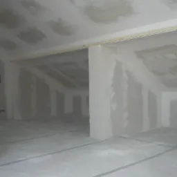 Poddasze w trakcie ocieplania, widoczne płyty gipsowo-kartonowe na ścianach i suficie, drewniana listwa montażowa, instalacja elektryczna w puszce.