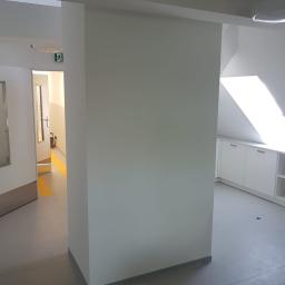 PEGAS Sp. z o.o. - Świeżo pomalowane na jasno szaro ściany w biurze, widoczny fragment korytarza z żółtymi pasami na podłodze i białe szafki w tle.