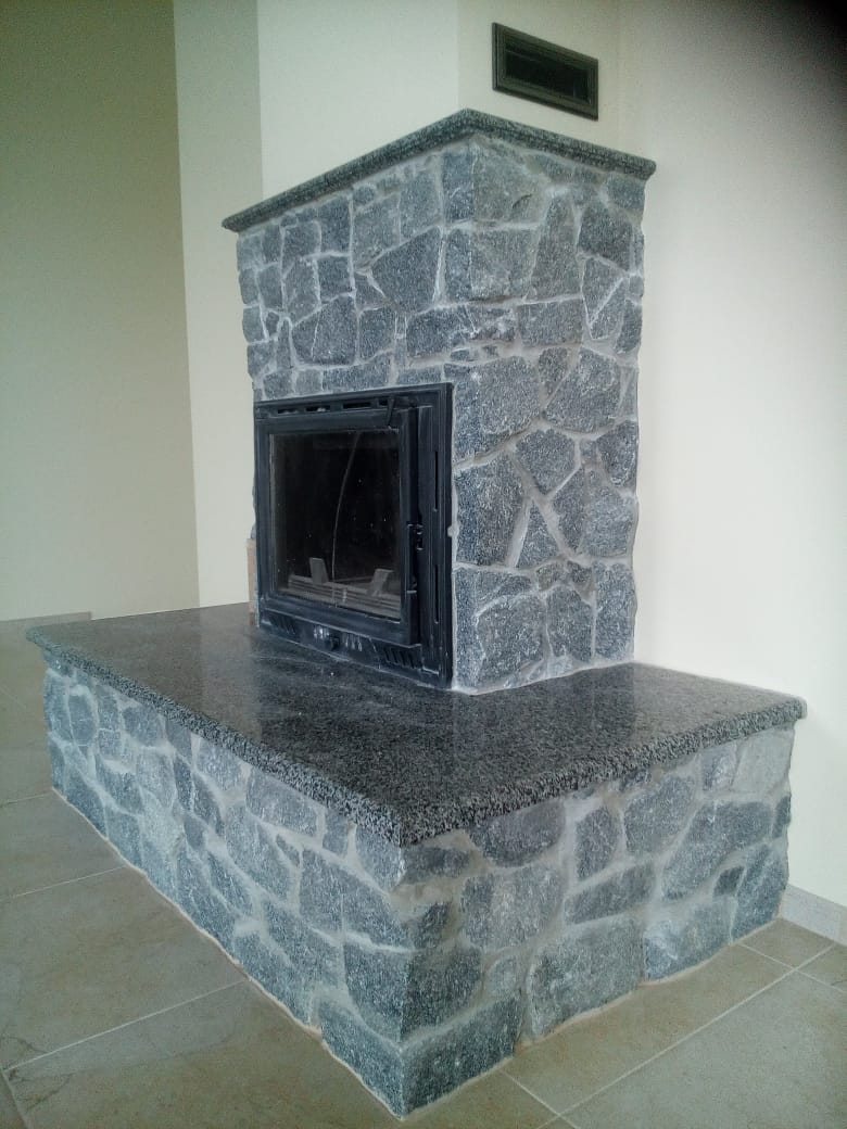 Obróbka kamieniarska kominka z szarego granitu, z widoczną fakturą kamienia i czarnym wkładem kominkowym.