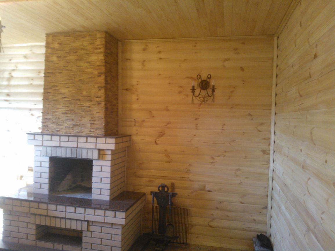 Komin z cegły i kamienia dekoracyjnego w drewnianym wnętrzu, widoczny ozdobny kinkiet i akcesoria kominkowe.