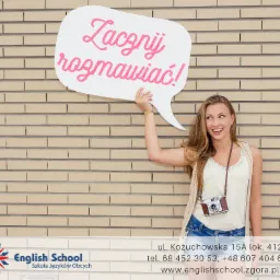 Uśmiechnięta młoda kobieta trzymająca dymek z napisem 'Zacznij rozmawiać!' na tle ceglanej ściany, w tle logo szkoły językowej.