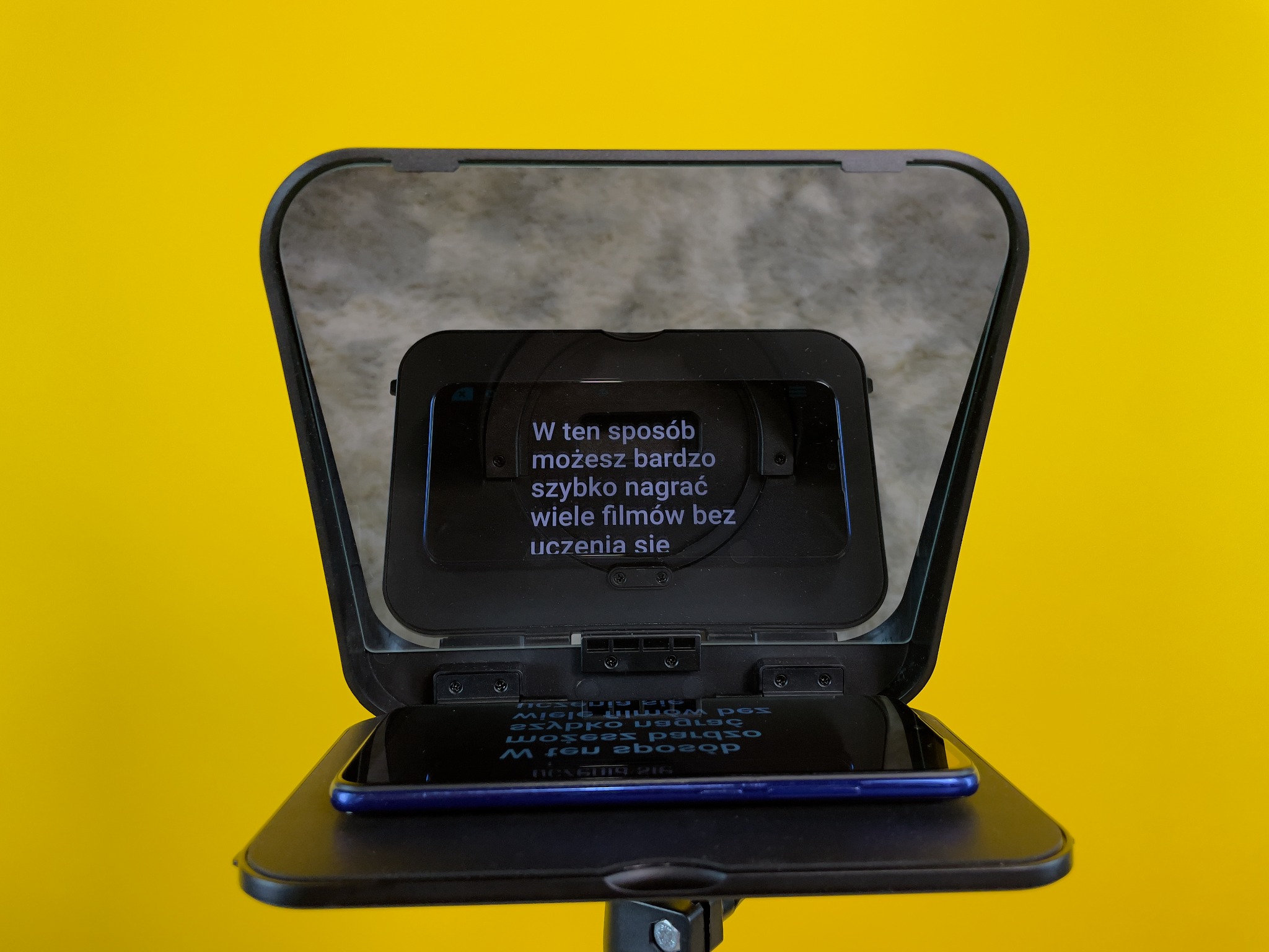 Teleprompter z zamontowanym smartfonem wyświetlającym tekst na lustrzanej szybie, na jaskrawożółtym tle.