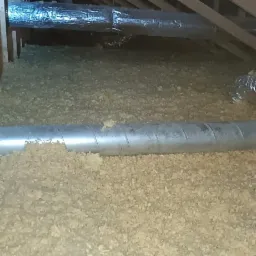 Poddasze z widoczną izolacją z wełny mineralnej między krokwiami oraz srebrnymi rurami wentylacyjnymi.