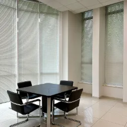 Nowoczesna sala konferencyjna z kwadratowym, czarnym stołem i czterema sk&oacute;rzanymi krzesłami na chromowanych nogach, oświetlona jasnym światłem z paneli sufitowych i naturalnym światłem wpadającym...