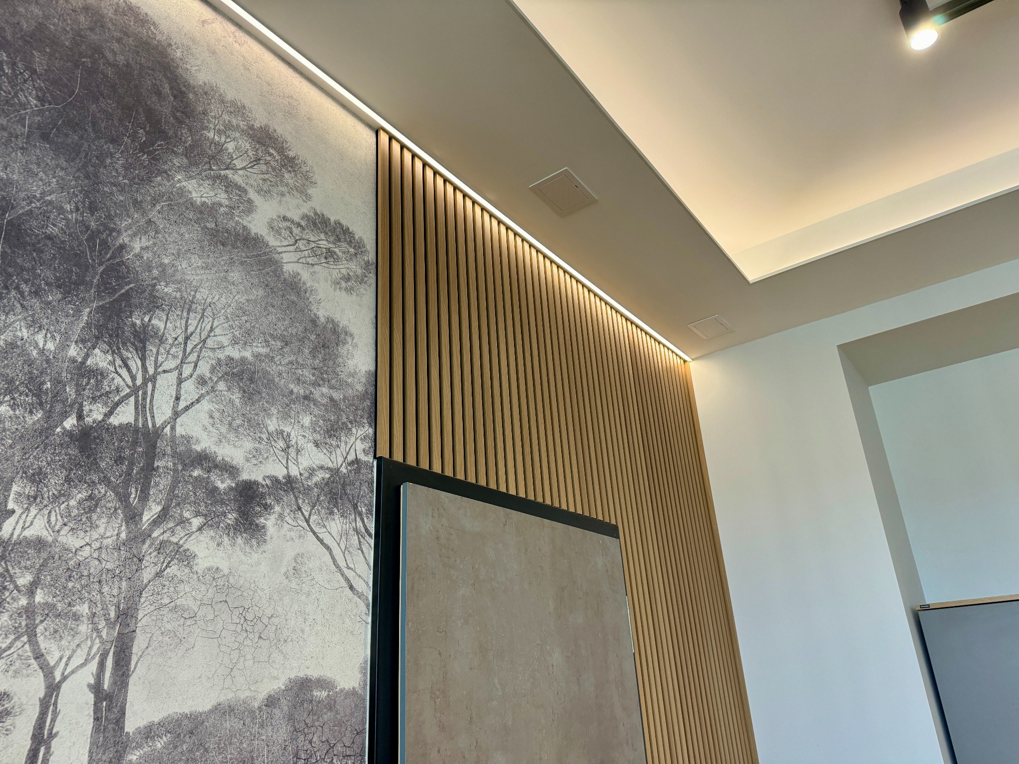 Ściana z drewnianymi lamelami, fototapetą z motywem drzew i oświetleniem LED w nowoczesnym wnętrzu.