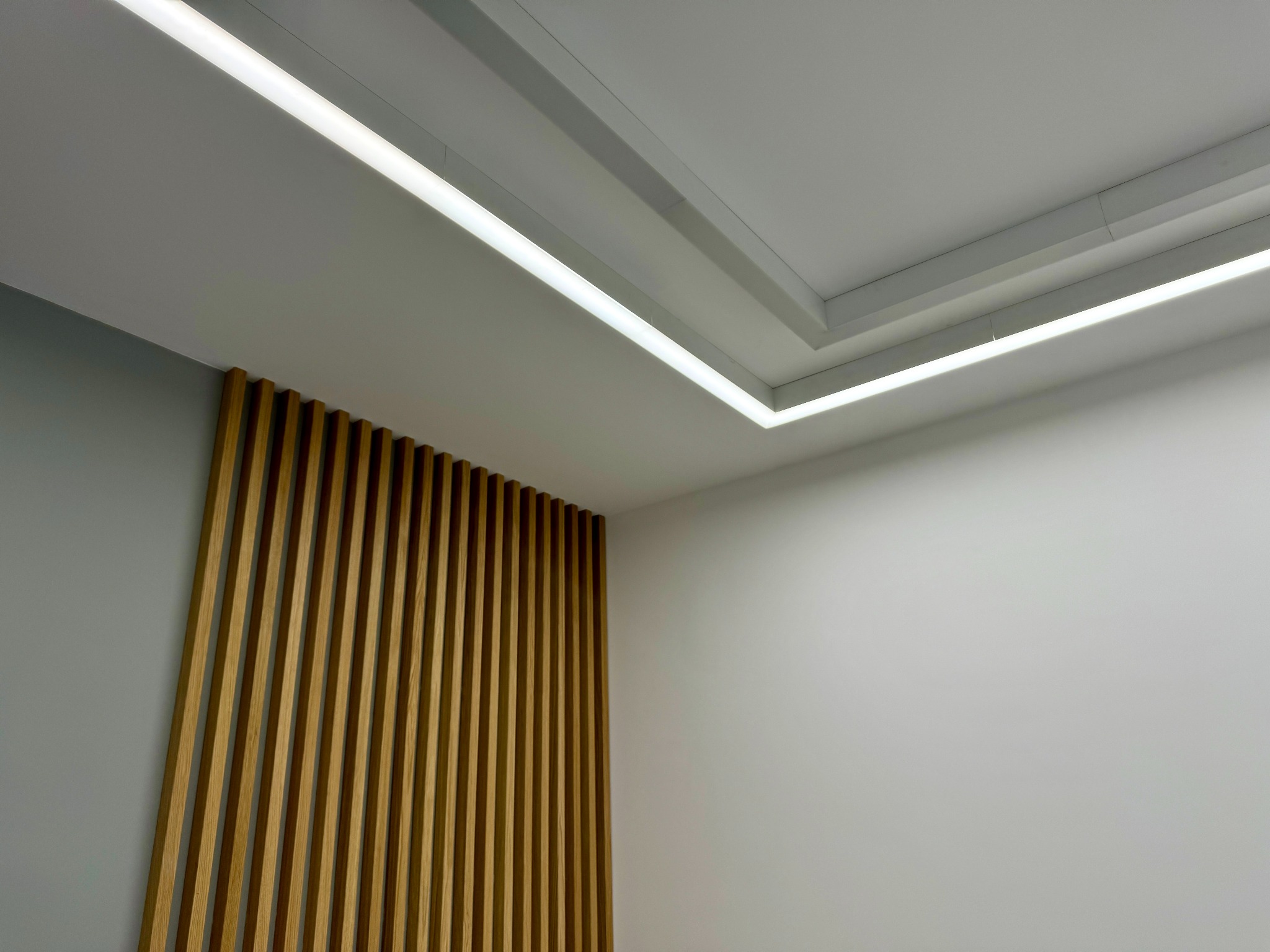 Nowoczesne oświetlenie sufitowe LED z drewnianą dekoracyjną ścianką działową z pionowych listew w minimalistycznym wnętrzu.