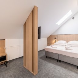 Bobieni Fotografia Wiesław Bobieni - Jasne wnętrze pokoju hotelowego na poddaszu z dwoma łóżkami, drewnianą ścianką działową i minimalistycznym oświetleniem.