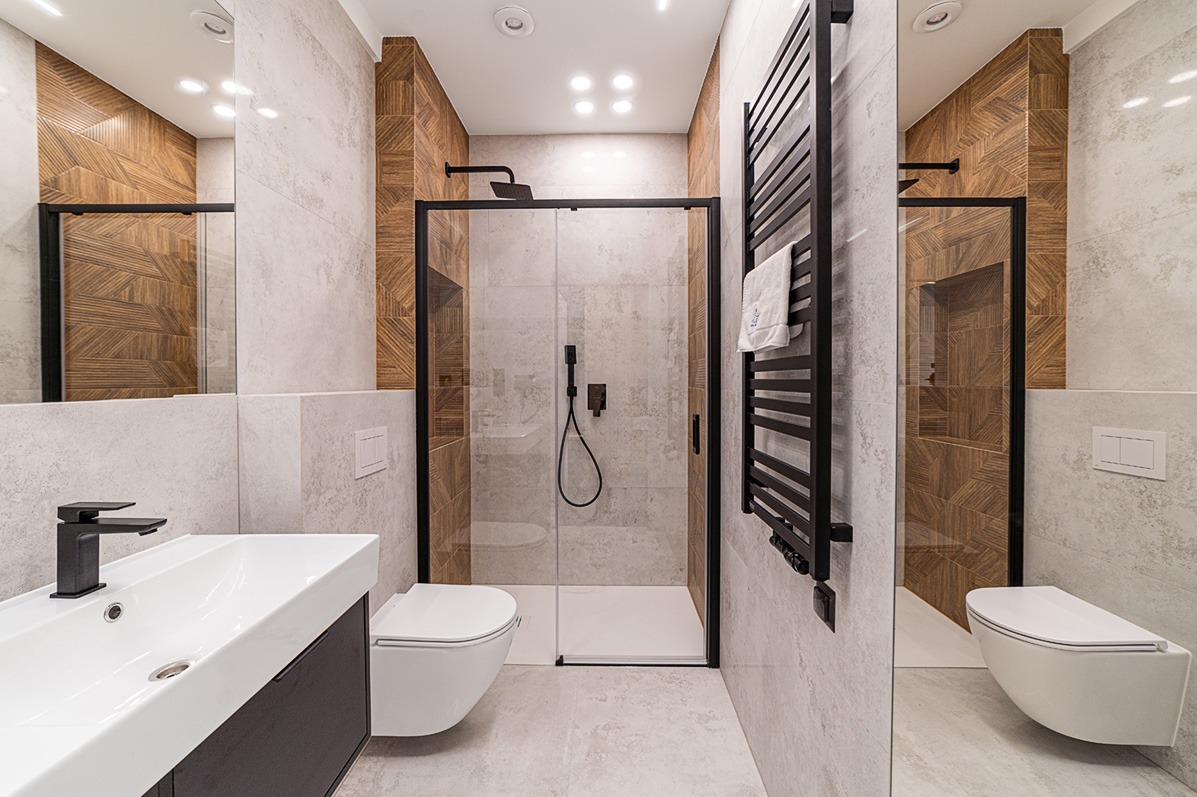 Nowoczesna łazienka z kabiną prysznicową typu walk-in, umywalką nablatową i grzejnikiem drabinkowym w czarnych ramach, wykończona płytkami w odcieniach beżu i brązu.