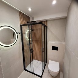 MÓJ SZEŚCIAN - Nowoczesna łazienka z kabiną prysznicową w czarnej ramie, podświetlanym okrągłym lustrem i płytkami w odcieniach szarości oraz drewnianymi lamelami na ścianie.