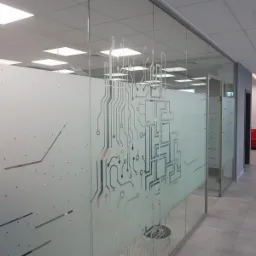 Przeszklona ściana działowa z matową folią dekoracyjną przedstawiającą schemat obwodu elektronicznego w nowoczesnym biurze.