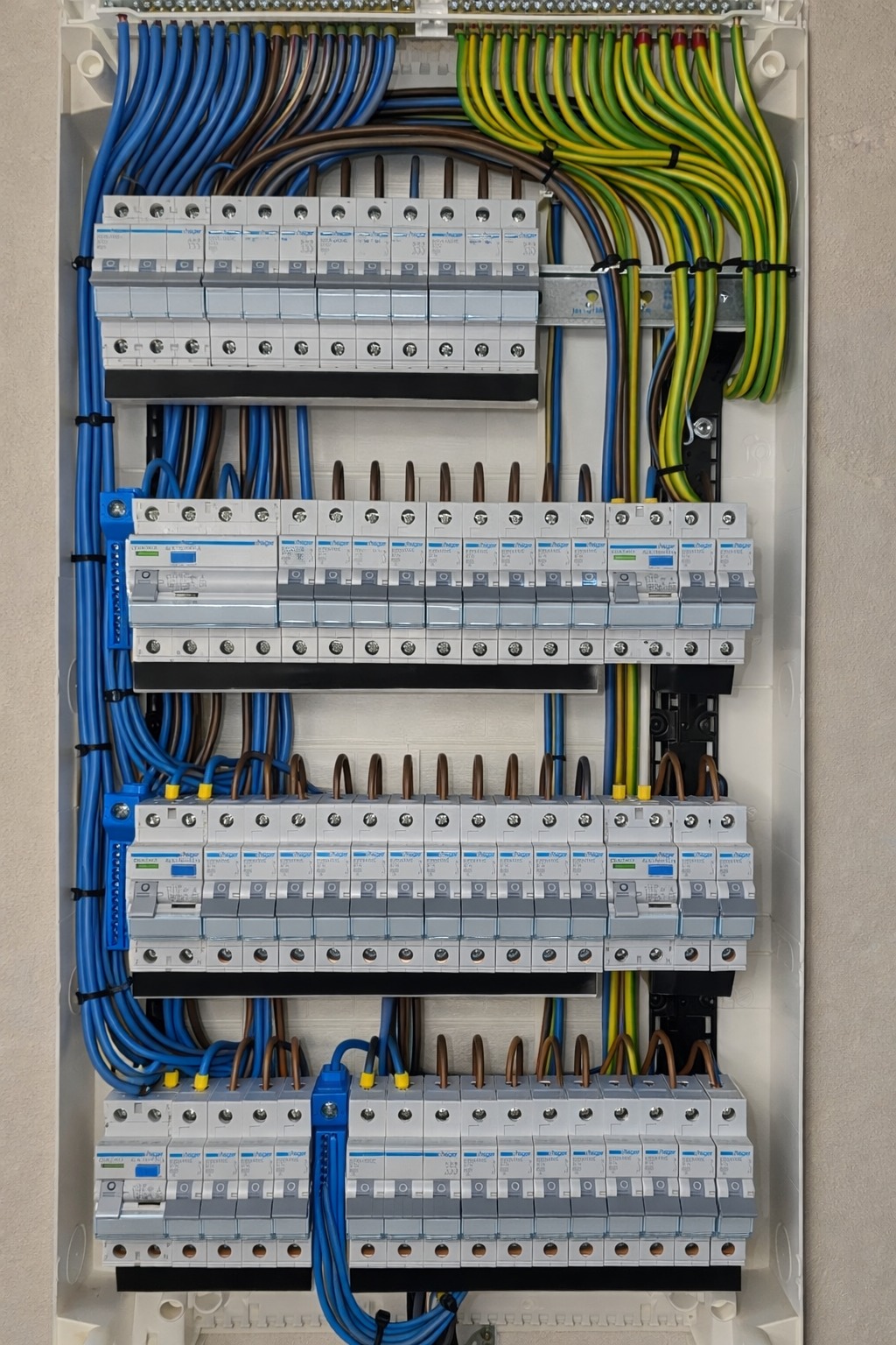Rozdzielnia elektryczna z precyzyjnie ułożonymi przewodami w kolorach niebieskim, brązowym i żółto-zielonym. Widoczne zabezpieczenia i listwy montażowe.