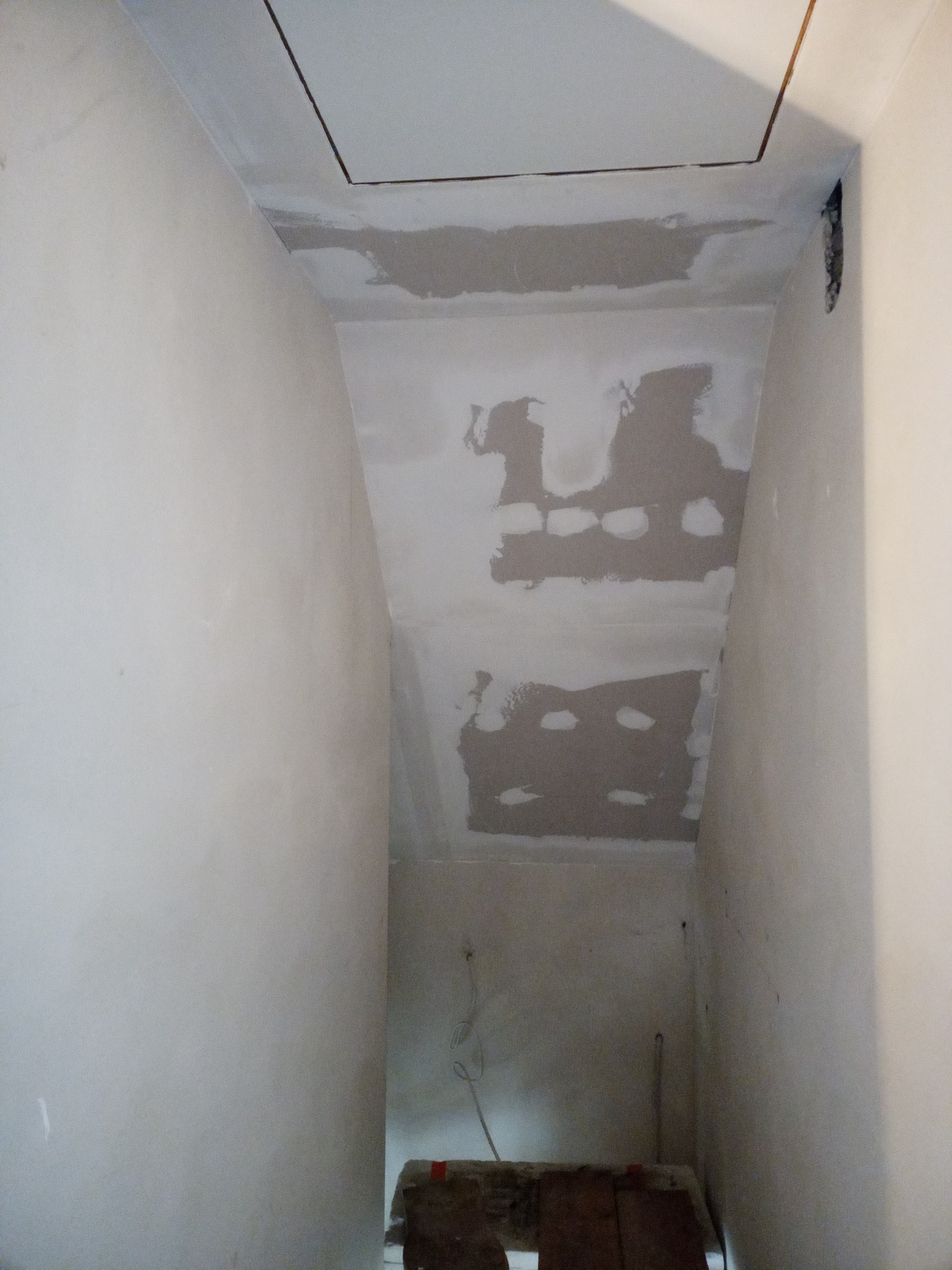 Fragment pomieszczenia w trakcie prac wykończeniowych; ściany i sufit częściowo pokryte szpachlą, widoczne nierówności i niedoskonałości przed malowaniem.