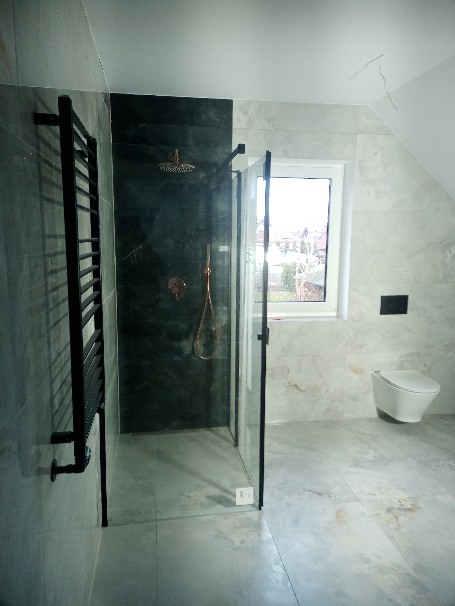 Wykończona łazienka w Biłgoraju z kabiną prysznicową typu walk-in z czarnymi detalami, grzejnikiem drabinkowym i toaletą w zabudowie, wykończona płytkami imitującymi marmur w odcieniach szarości...