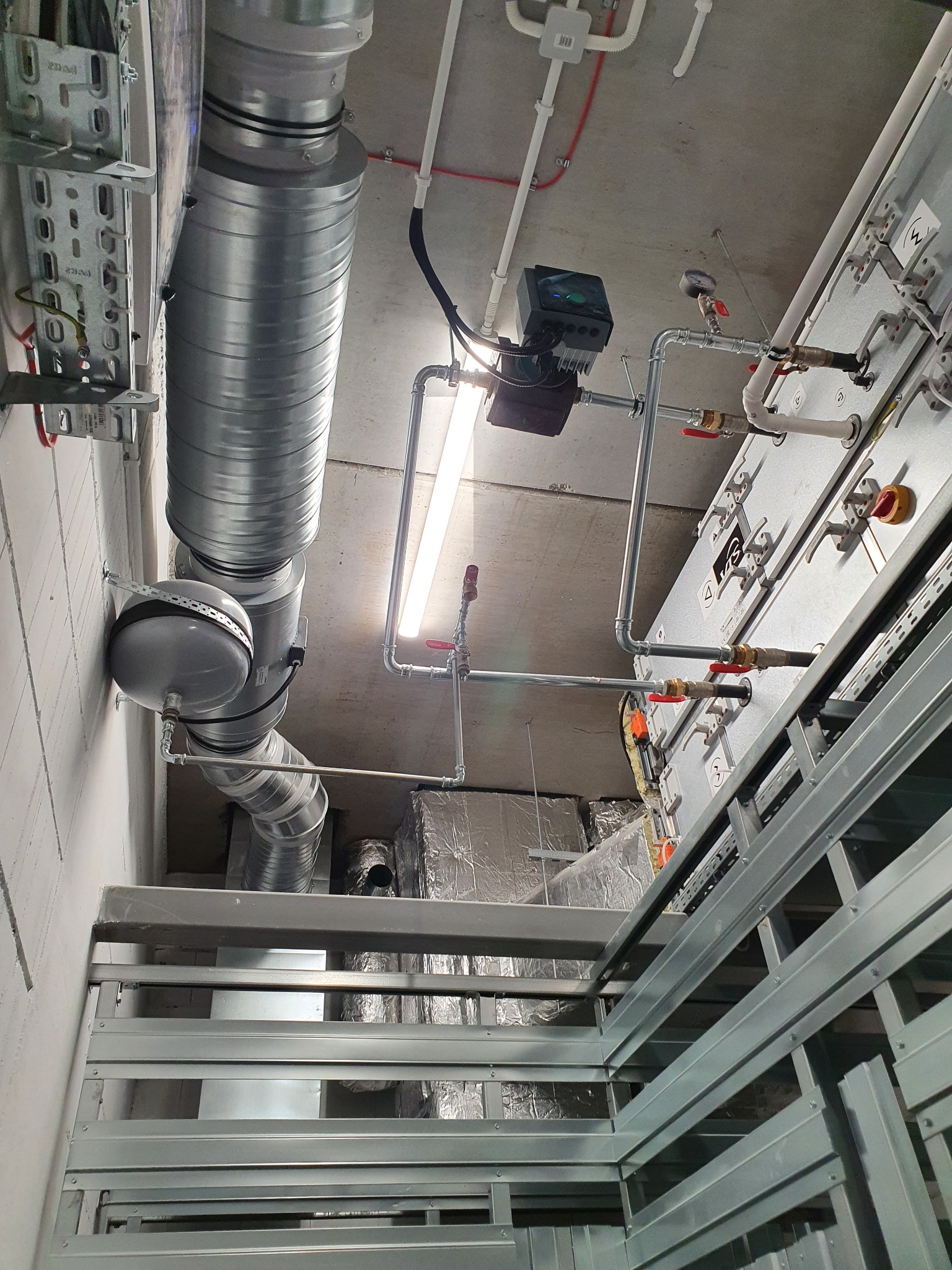 Instalacja centralnego ogrzewania z rurami, zaworami i pompą obiegową zamontowana w Oławie, widok z dołu na sufit z oświetleniem LED.