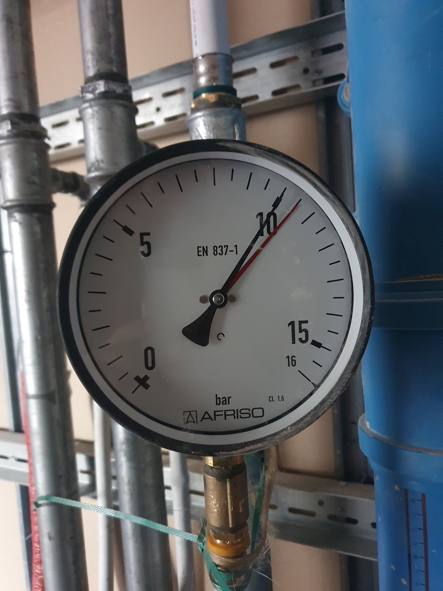 Manometr AFRISO wskazujący ciśnienie w instalacji, zamontowany na rurach w pomieszczeniu technicznym.