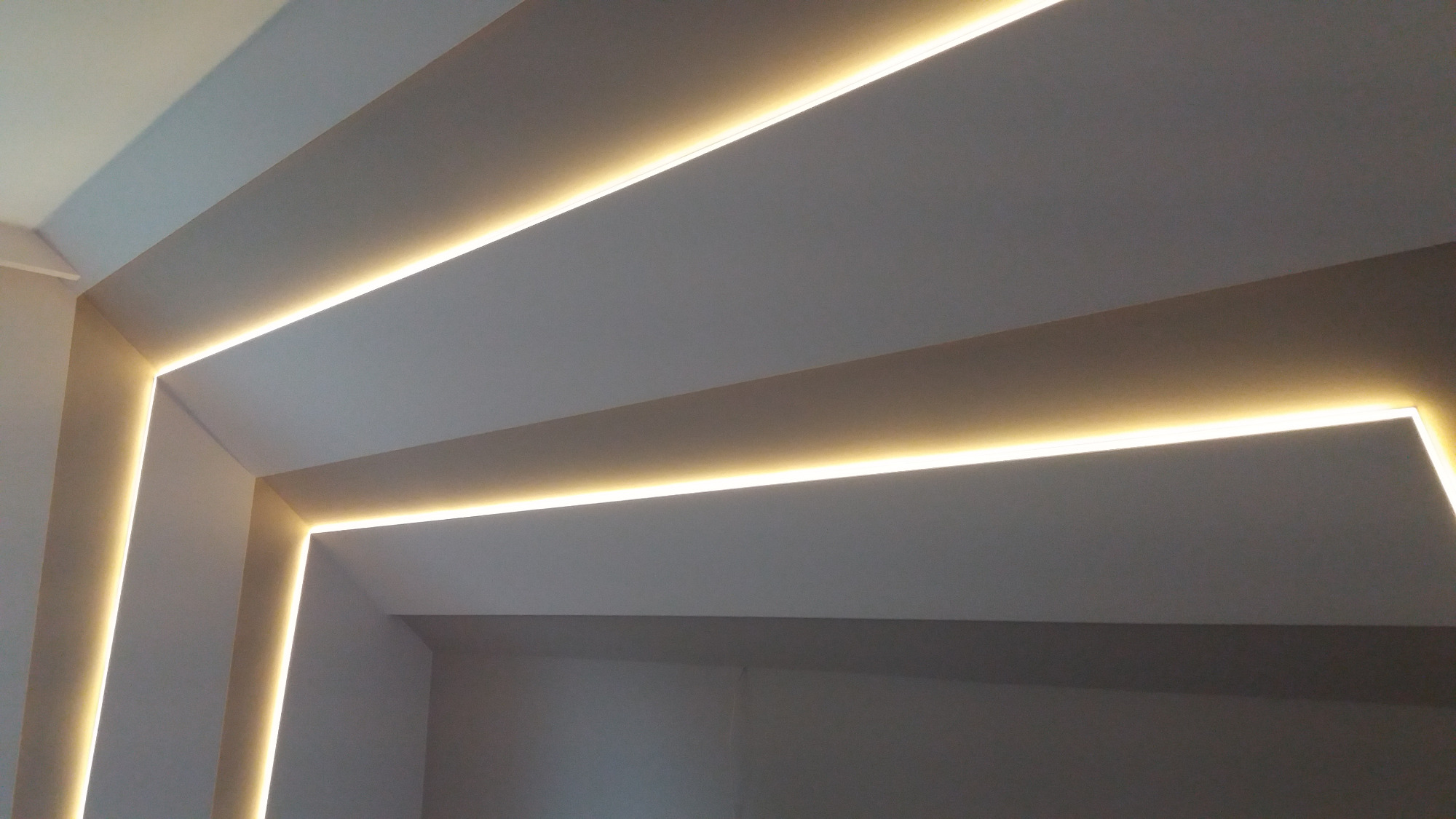 Nowoczesny sufit z wbudowanym oświetleniem LED, tworzącym geometryczne wzory w jasnym, minimalistycznym wnętrzu.