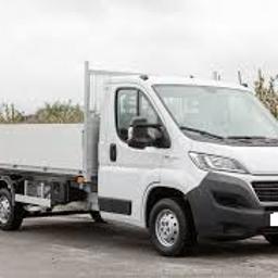 Piokop - Biały samochód dostawczy typu wywrotka z otwartą skrzynią ładunkową, zaparkowany na poboczu drogi, w tle drzewa owocowe z białymi kwiatami i pochmurne niebo.