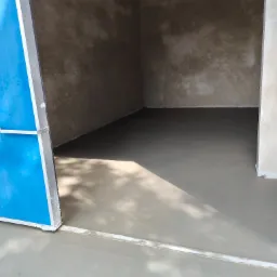 Wnętrze pomieszczenia z wylewką jastrychową, widoczne ślady po niebieskich drzwiach, świeżo wykonana, gładka powierzchnia, surowe ściany w tle.