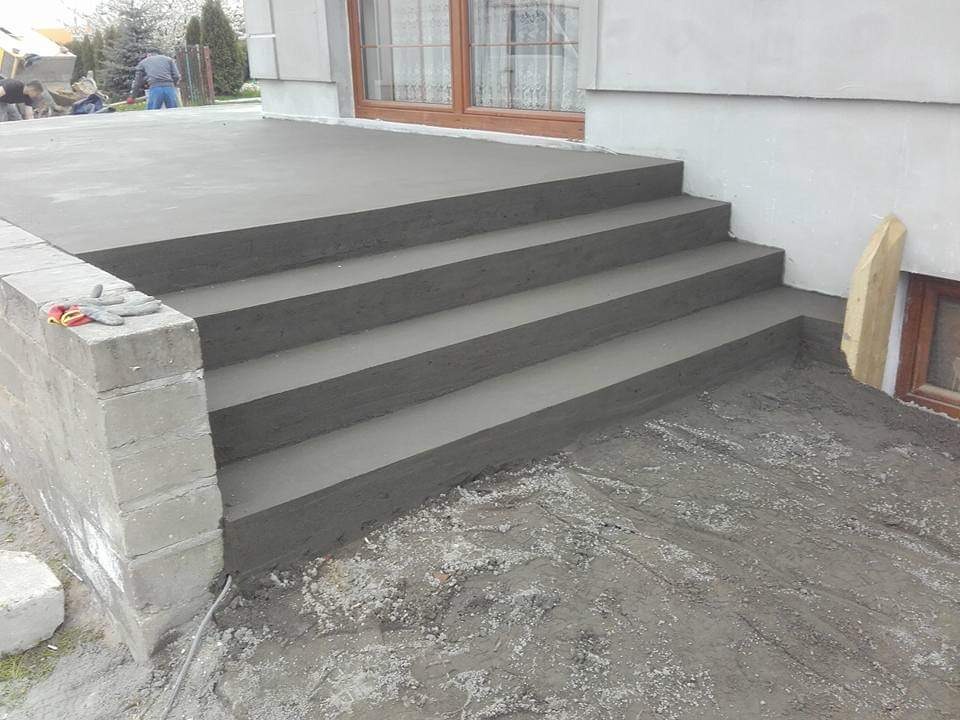 Świeżo wylane betonowe schody wejściowe do domu, widoczne ślady szalunku, na murku leżą robocze rękawice.