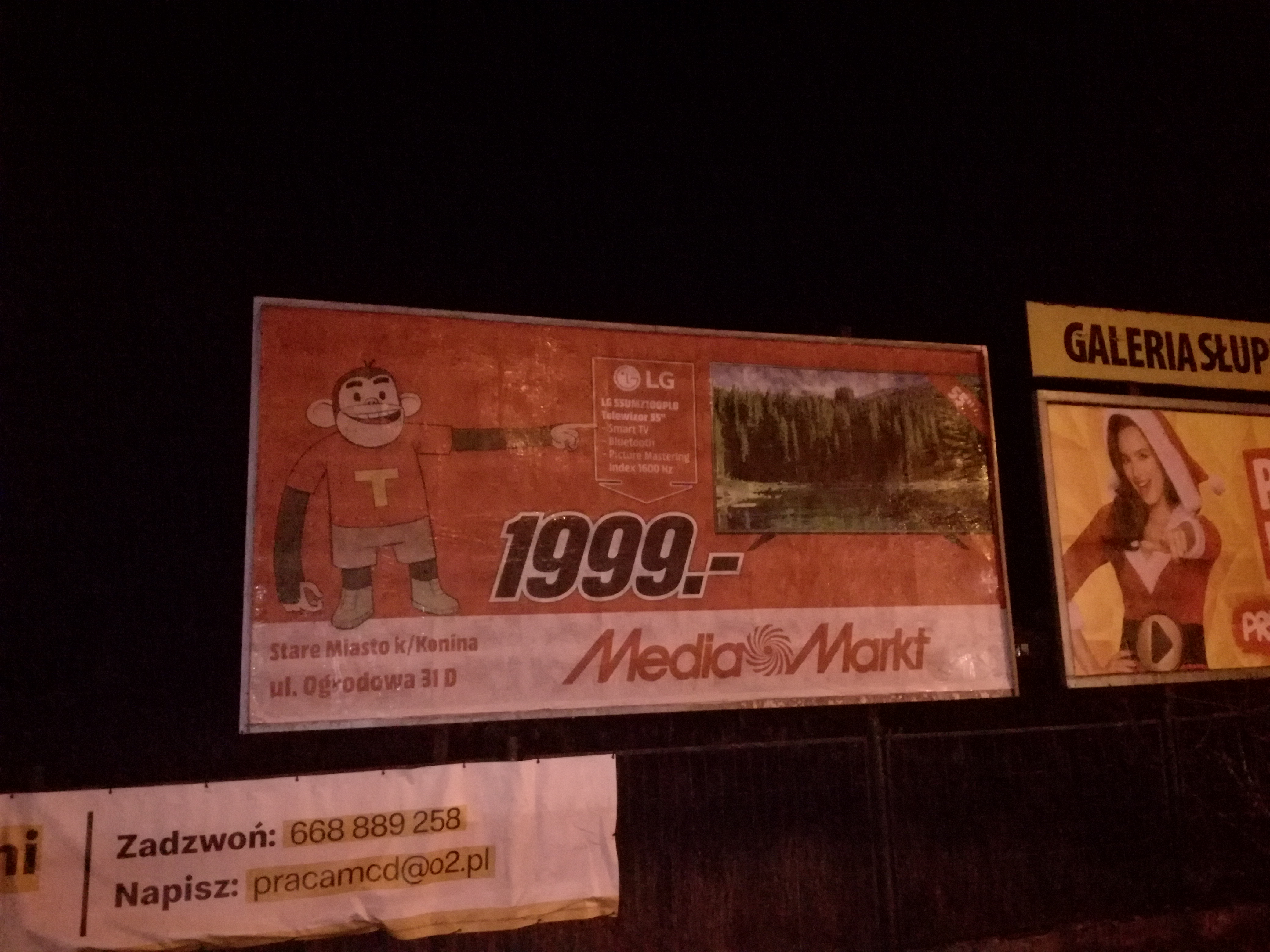 Billboard reklamowy Media Markt prezentujący telewizor LG 55 cali w cenie 1999 zł, obok inny billboard z kobietą w stroju Mikołajki.