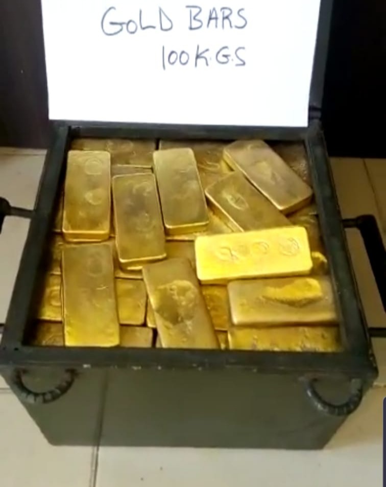 Szkatułka wypełniona sztabkami złota o wadze 100 kg, widoczna kartka z napisem 'Gold Bars 100 KGS'.