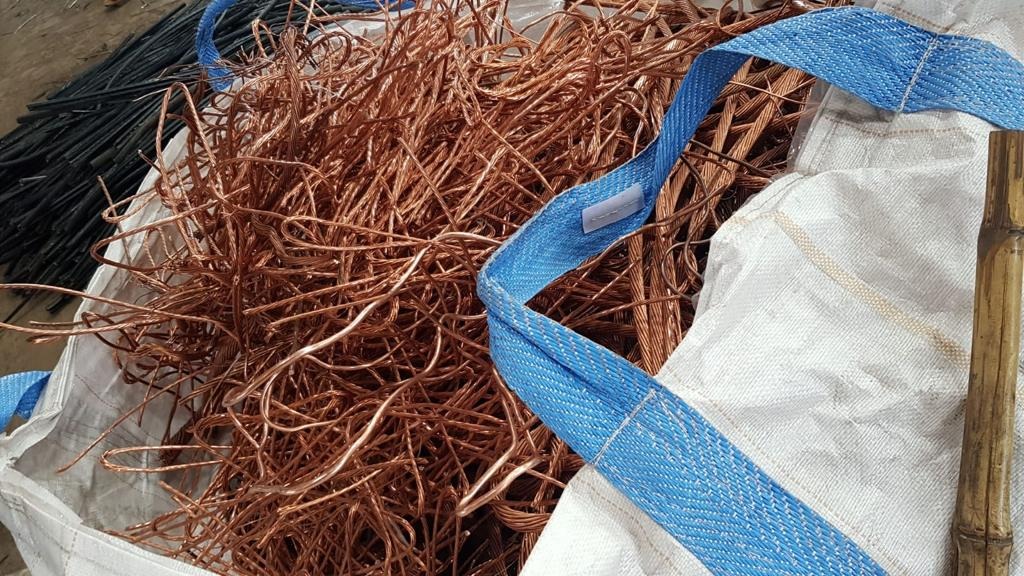 Odzyskana miedź w worku typu big bag z niebieskimi uchwytami, obok leżą czarne kable.