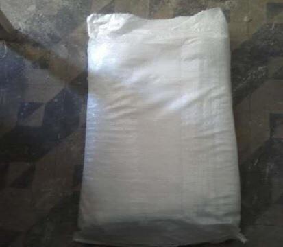 Worek z białym cukrem ICUMSA 45 leżący na podłodze z szaro-czarną mozaiką.