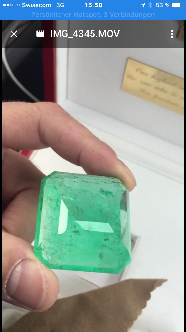 Szlifowany, surowy szmaragd w dłoni, o wyraźnych inkluzjach i geometrycznym kształcie, prezentowany na jasnym tle z fragmentem tekstu w tle.