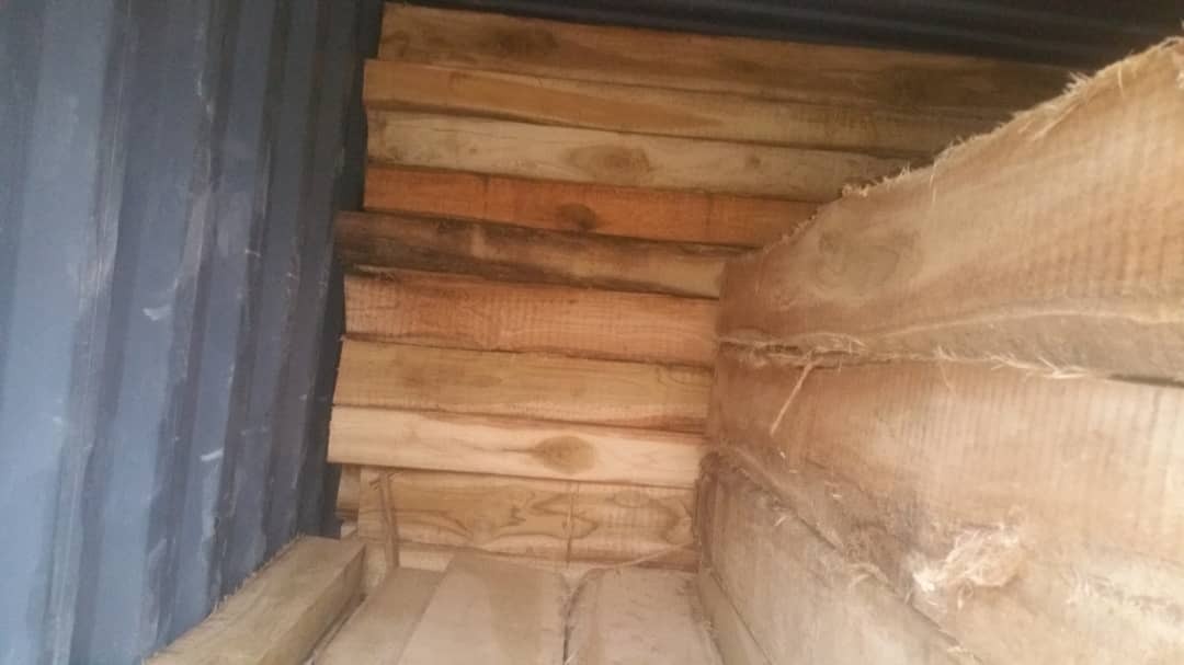Stos drewnianych belek wewnątrz kontenera transportowego, widoczne ślady wilgoci na niektórych elementach.