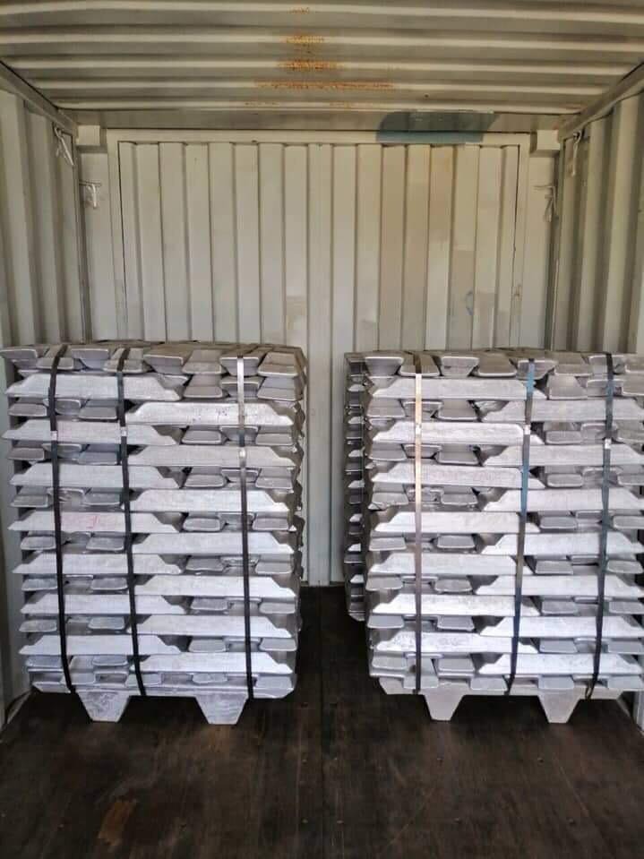 Dwie palety z sztabami aluminium, zabezpieczone czarnymi taśmami, umieszczone w kontenerze transportowym.