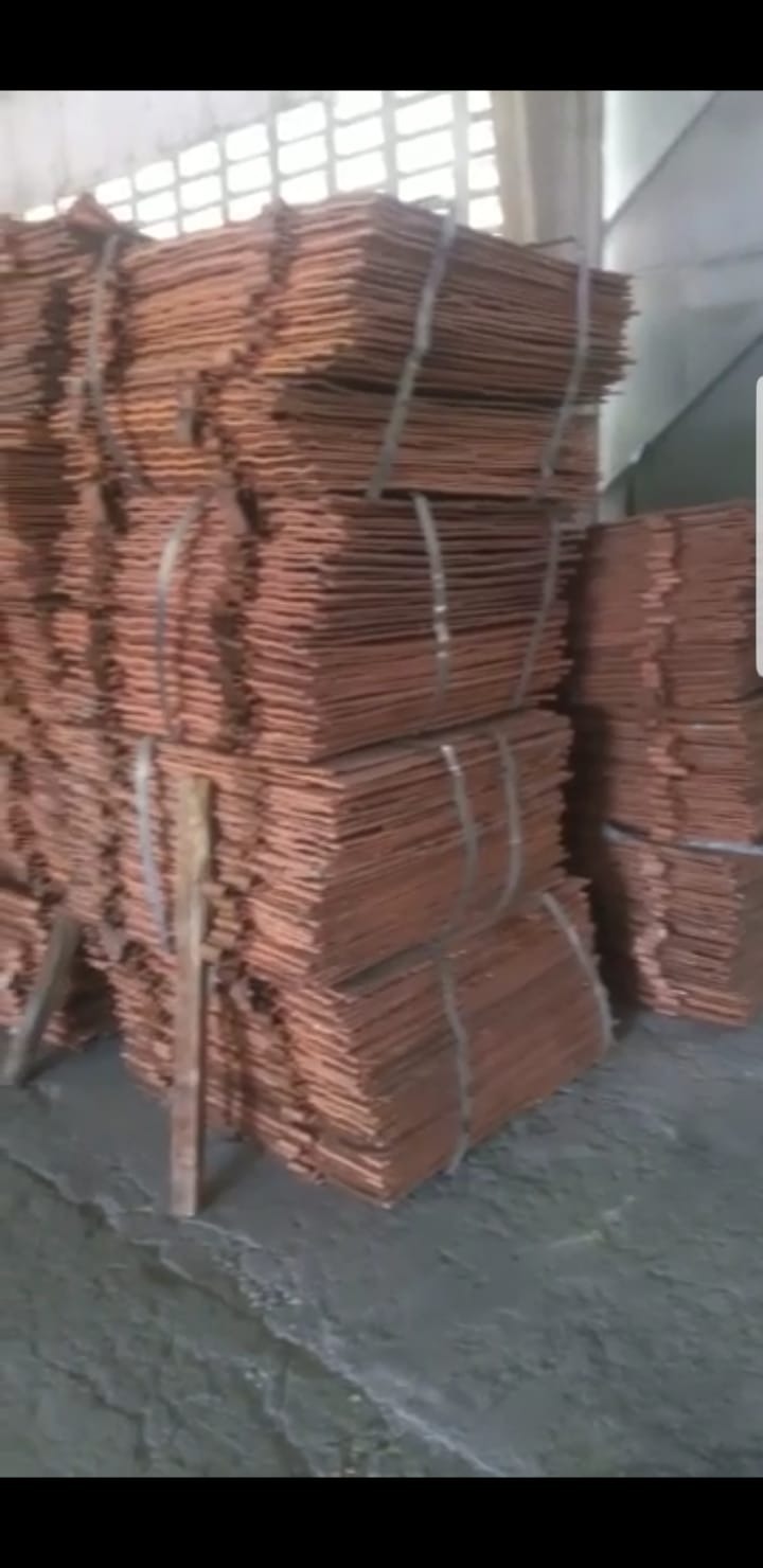 Stosy arkuszy miedzi wiązane taśmami, składowane w magazynie; widoczne niedoskonałości powierzchni arkuszy.