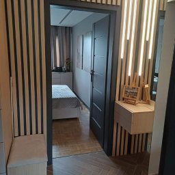 FHU ANMEBEL - Nowoczesna aranżacja przedpokoju z drewnianymi lamelami na ścianach, siedziskiem z tapicerowanym wiekiem i otwartymi drzwiami do sypialni z parkietem w jodełkę.