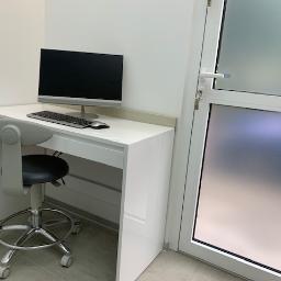 FHU ANMEBEL - Białe biurko z komputerem i krzesłem na kółkach, minimalistyczne wnętrze z matowymi szklanymi drzwiami.