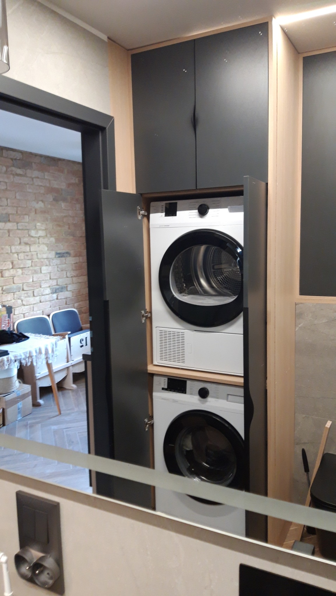 Pralka i suszarka w zabudowie meblowej z czarnymi frontami, widoczne przez lustro w łazience.