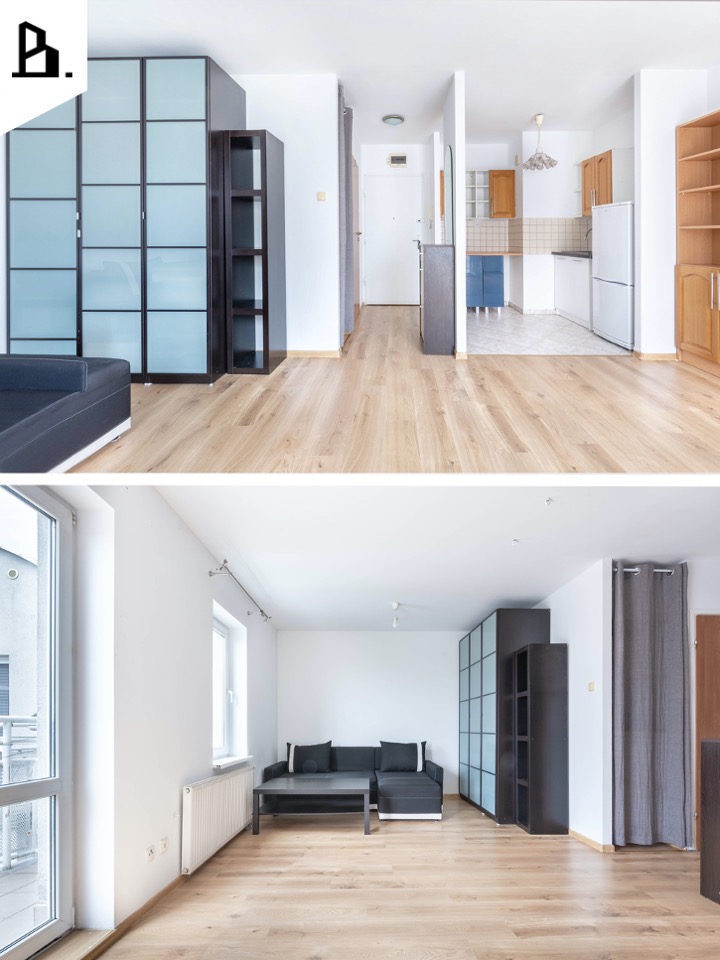 Jasne, przestronne wnętrze mieszkania z parkietem, widok na salon z ciemnoszarą sofą i stolikiem kawowym oraz kuchnię w tle z białymi i drewnianymi szafkami.